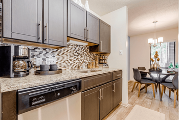 A kitchen with a black dishwasher and brown cabinets.