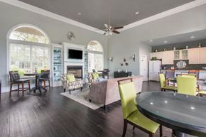 Riverview apartment for rent - Clubhouse Seating Area with Large Windows on either side of Fireplace with TV and Shelves Surrounding Fireplace Multi Colored Accent Chairs Grey Couch and Dining Room Tables with Green Chairs and Clubhouse Kitchen in the Background