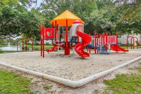 Riverview apartment for rent - Blue Red and Yellow Playground on Sand with Building Exterior and Treeline in the Background
