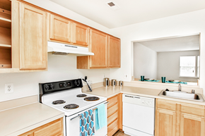 Fredericksburg apartment for rent - Kitchen with tile floors, white appliances, and wood cabinets. Living room in background with large window.