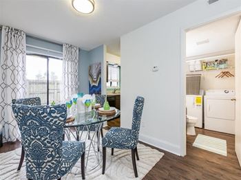 Furnished model dining room with glass dining table and chairs on area rug next to utility closet with washer and dryer