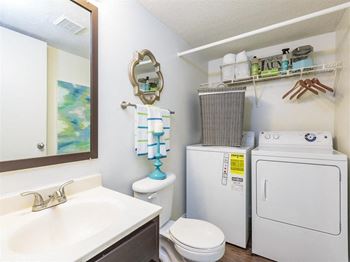 Model bathroom with washer and dryer below wire shelf with decorations and supplies