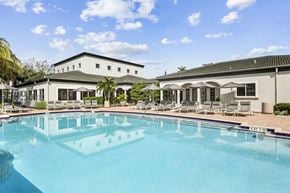Davie apartment for rent - a swimming pool with lounge chairs and umbrellas in front of a white building
