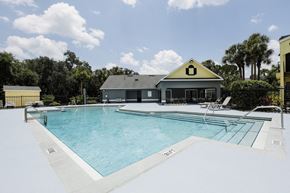 Sanford apartment for rent - Community pool with sundeck, lounge chairs, surrounded by black metal fence with trees, and building exteriors in the background
