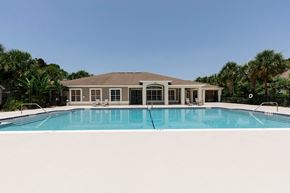 Bradenton apartment for rent - Community pool with sundeck, lounge chairs, surrounded by black metal fence with trees in the background