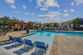 Pflugerville apartment for rent - A pool area with blue chairs and a wooden pergola.