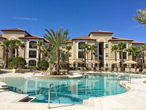 Kissimmee apartment for rent - a large swimming pool with palm trees in front of a building