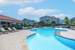 Austin apartment for rent - A large outdoor swimming pool surrounded by lounge chairs and umbrellas.