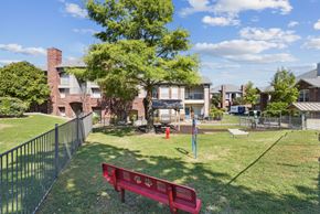 San Antonio apartment for rent - A red bench with a logo on it is in the foreground of a grassy area.