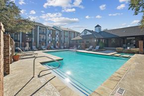 Euless apartment for rent - A swimming pool surrounded by a brick wall and a building in the background.