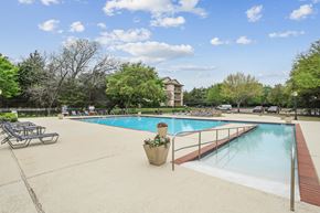 Dallas apartment for rent - A large outdoor swimming pool surrounded by trees and a building in the background.