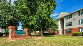 Hampton apartment for rent - Community Entrance Sign on Grass in Front of Tree Line and next to and aparmtent builing
