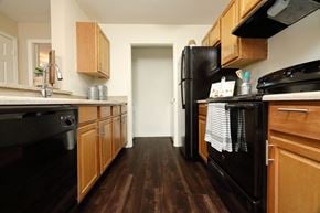 St. Augustine apartment for rent - The B1 Kitchen has light oatmeal-colored countertops with light wood cabinetry. Black kitchen appliances contrast against the light paint. An open closet at the end of the galley-style room holds the full-size washer and dryer appliances.