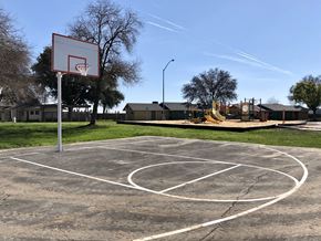 Fresno apartment for rent - A basketball court with a hoop and a playground in the background.