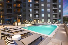 Denver apartment for rent - A large swimming pool with sun loungers and a striped bean bag in front of a large apartment block.