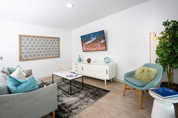 Seattle apartment for rent - A living room with a grey couch, a white side table, a blue chair, and a painting on the wall.