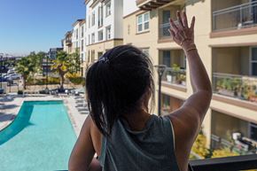 Fremont apartment for rent - a woman standing on a balcony overlooking a swimming pool with her hand in the air