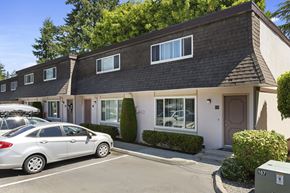 Edmonds townhouse for rent - Side View of Townhome Buildings with White Walls, Manicured Shrubs, and Resident Reserved Parking at Woodlake Townhomes, Washington