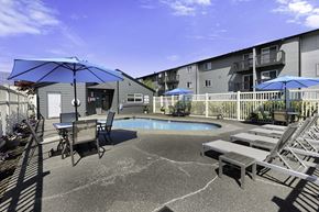 Edmonds apartment for rent - a patio with a pool and chairs and umbrellas at Pacific Park Apartment Homes, Washington