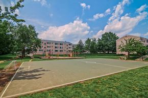 Herndon apartment for rent - A basketball court is surrounded by grass and trees in front of a building at Dulles Glen Apartments, Herndon, Virginia