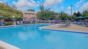 Leesburg apartment for rent - A large swimming pool with a blue tiled edge and a sun lounger area with blue sunshades.