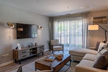 Mundelein apartment for rent - A well-lit living room with a wooden coffee table and a large window with curtains.