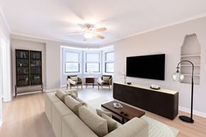 Chicago apartment for rent - A living room with a large couch, a flat screen TV, and a ceiling fan.
