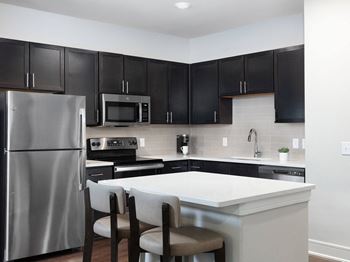 Kitchens feature quartz countertops, ceramic tile backsplashes, stainless steel appliances, shaker-style cabinetry, and chrome hardware