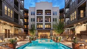 Phoenix apartment for rent - A large swimming pool is surrounded by potted plants and lounge chairs in the middle of a courtyard.