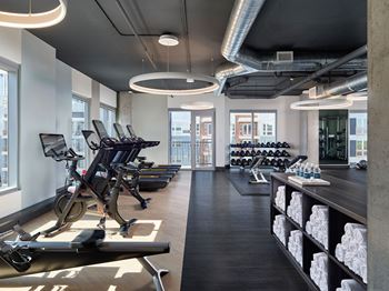 24/7, Industrial-inspired fitness center with state-of-the-art cardio and strength equipment, and large windows boasting dynamic city views