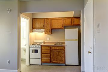 Lansing triplex for rent - A kitchen with wooden cabinets and white appliances.