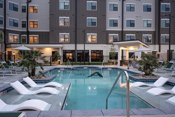 A swimming pool with white chairs in front of a building