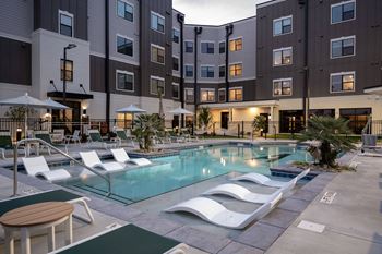 A swimming pool with lounge chairs in front of an apartment building