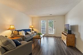 Augusta townhouse for rent - A living room with a grey couch, a wooden coffee table, a lamp, a TV, and a window with a view of trees.