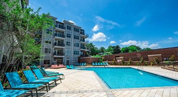 A swimming pool surrounded by blue lounge chairs and apartment buildings.
