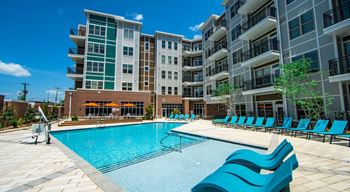 A large swimming pool with blue lounge chairs in front of apartment buildings.