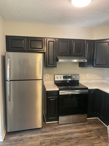 A kitchen with black cabinets and a stainless steel refrigerator