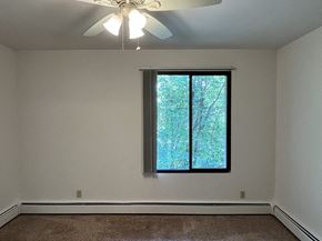 Milwaukee apartment for rent - A room with a ceiling fan and a window showing trees outside.