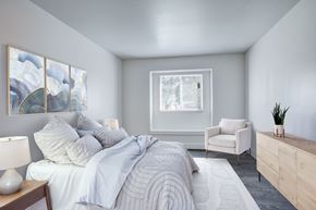 Fort Collins apartment for rent - A bedroom with a large bed, a white chair, and a painting on the wall.