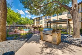Dallas apartment for rent - A BBQ grill is in the middle of a sandy area with a building in the background.