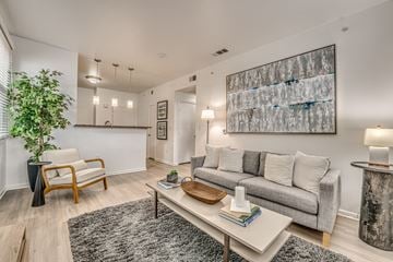 Dallas apartment for rent - A living room with a grey couch, a wooden chair, a coffee table, and a large abstract painting on the wall.
