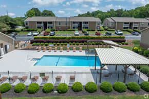 Simpsonville apartment for rent - A swimming pool surrounded by a fence and bushes in front of a building.