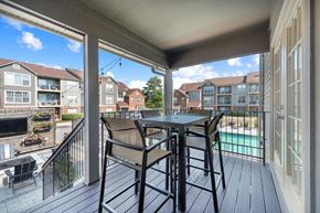 Lisle apartment for rent - A patio with a table and chairs overlooks a pool and apartment buildings.