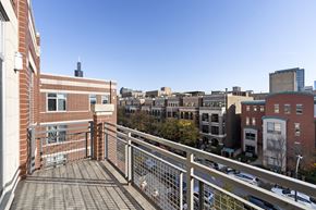 Chicago apartment for rent - A balcony with a metal railing overlooks a parking lot and buildings.