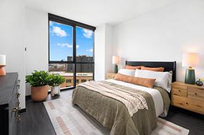Chicago apartment for rent - A bedroom with a large bed and a view of the city through the window.