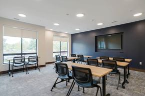 Lincoln townhouse for rent - Conference room with light wood tables, mesh chairs, large windows with shades, and wall-mounted TV, offering natural light and open layout.