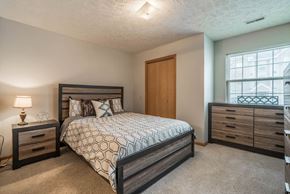 Omaha apartment for rent - A bedroom with a large bed, a nightstand with a lamp, and a nook with a large window