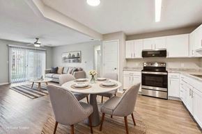 Lincoln apartment for rent - Virtually staged open-concept apartment kitchen and living area with white cabinetry, stainless steel oven, wood-style flooring, and sliding glass doors.