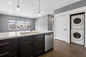 Omaha apartment for rent - Stacked in-home laundry sits just off the kitchen, beside a dark cabinet island with a deep sink, dishwasher, and pendant lights.