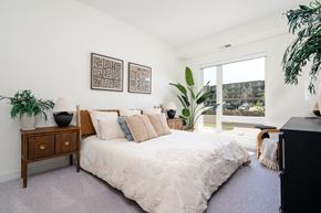 Eagan townhouse for rent - bedroom with king sized bed with off white linens , large window, and large plant in corner of room